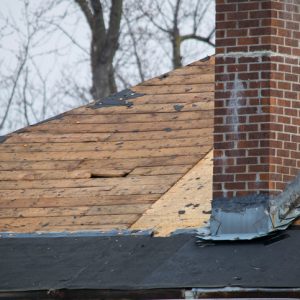 Roof of a residential house showing damage, multiple layers of shingles, missing shingles